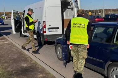 Funkcjonariusze Straży Granicznej kontrolują pojazdy na parkingu lub przy przejściu granicznym.
